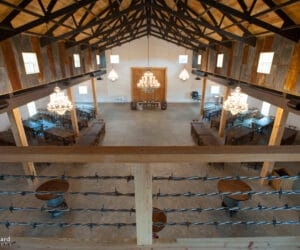 looking down from balcony at large indoor barn with wood beams and crystal chandeliers